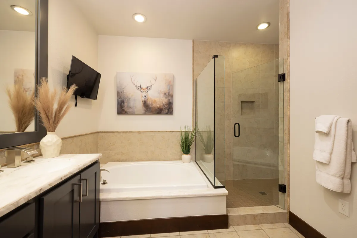 A tranquil bathroom with a soaking bathtub, walk-in shower enclosure, stylish vanity mirror, and tasteful deer artwork. The soft lighting and muted colors create a serene spa-like environment ideal for relaxation and renewal.