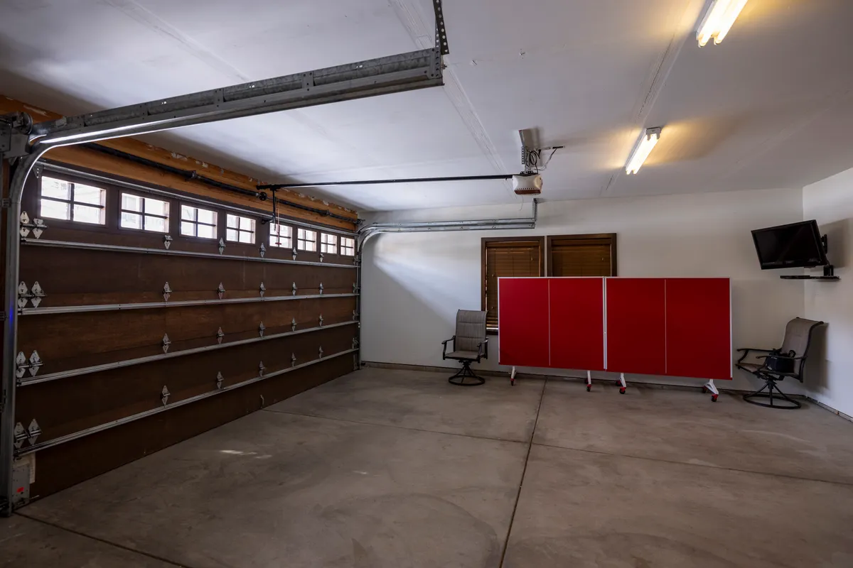 This image shows a garage area with a prominent red storage unit, garage door, flat-screen TV, and a seating area. The space is clearly designed for storage and organization, making it suitable for stashing bikes or larger equipment post-adventure.