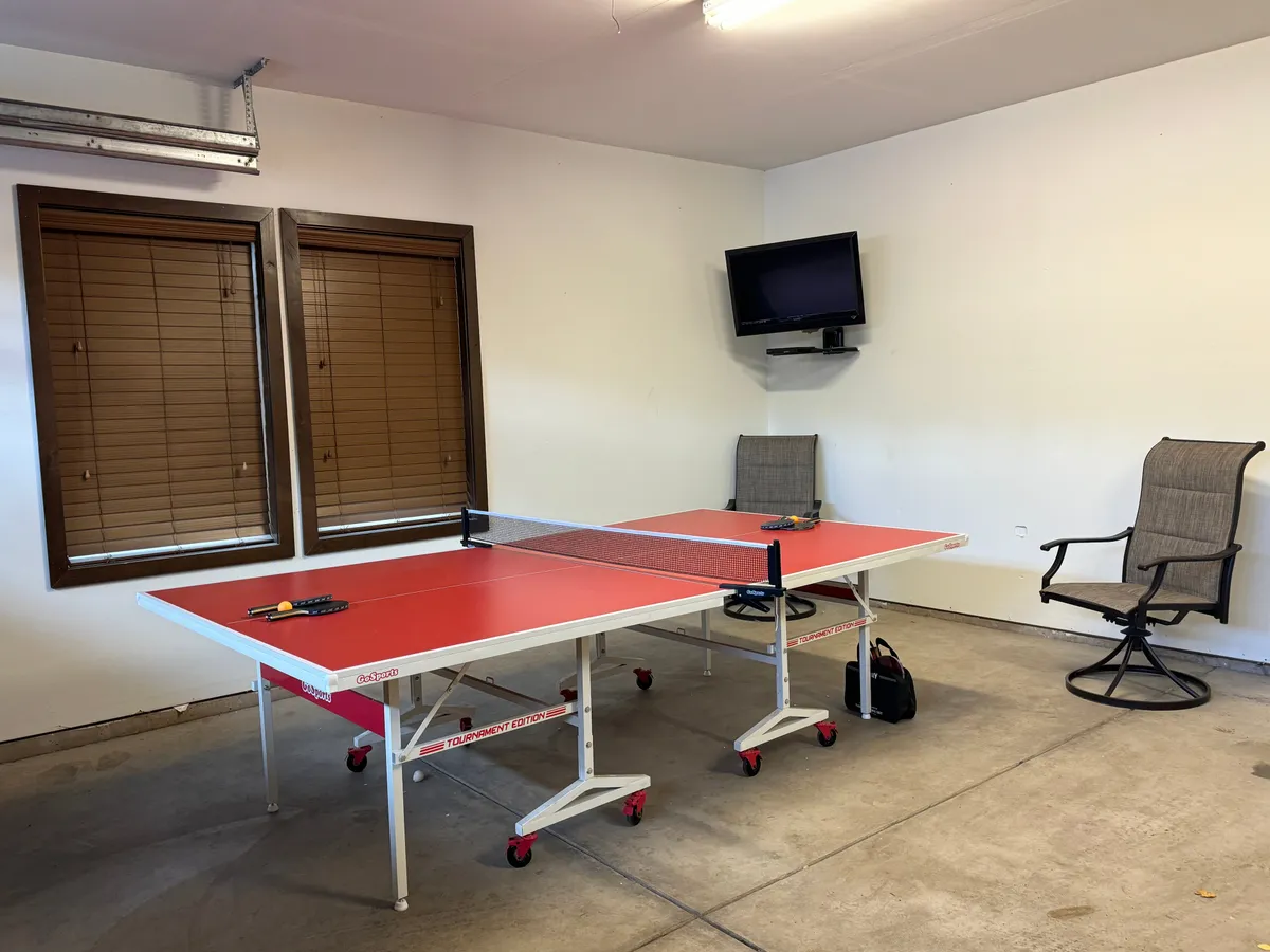An interior recreation space with a ping pong table as the centerpiece, surrounded by comfortable seating, a television, and large windows. The layout encourages a playful, social atmosphere ideal for both active games and relaxed downtime.