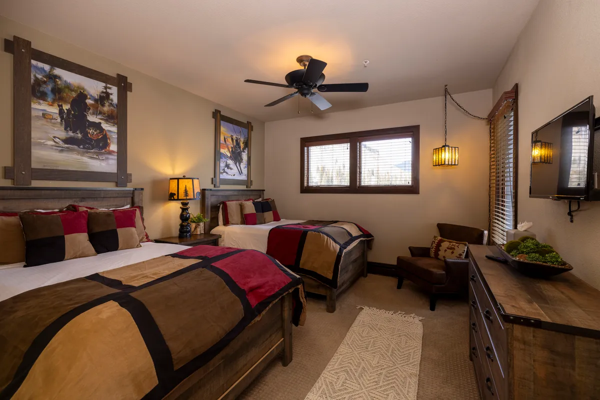 A welcoming bedroom with two beds adorned in colorful bedding, large artwork on the walls, and warm wooden furniture. The room is bright and spacious, perfect for families or groups seeking a cheerful place to recharge.