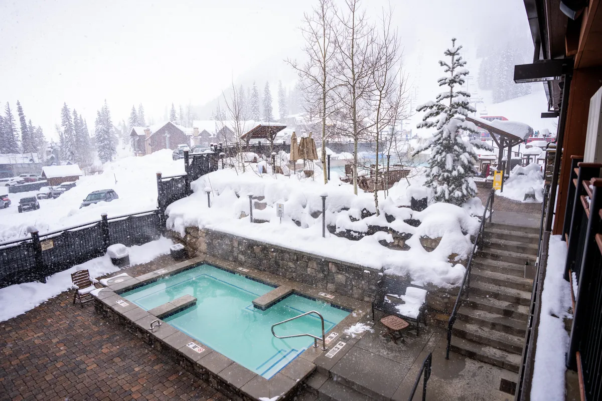 This exterior shot showcases a private outdoor hot tub surrounded by a snow-covered landscape and trees, with steps leading up and an inviting, serene atmosphere. The tub is positioned to maximize views and the sense of relaxation, with hints of starry nights or snowy evenings enhancing the appeal.
