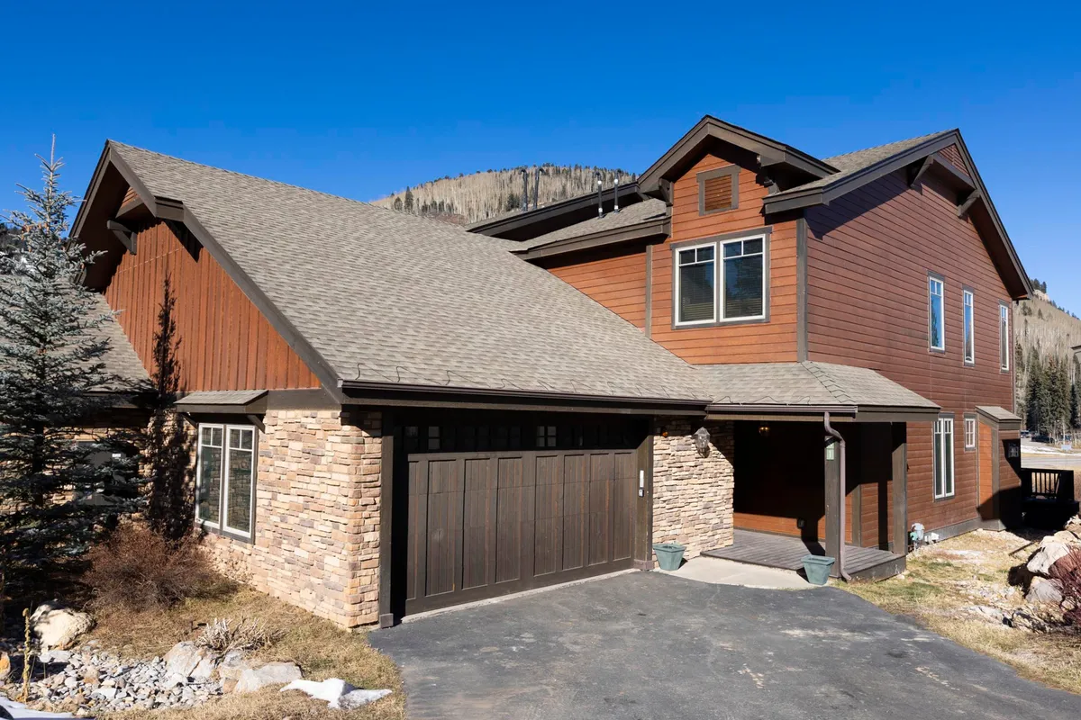 This exterior image shows the welcoming townhome front, complete with a wooden exterior, stone accents, garage, and cozy front porch. The mood is warm and inviting, suggesting comfortable homecomings after days spent exploring.