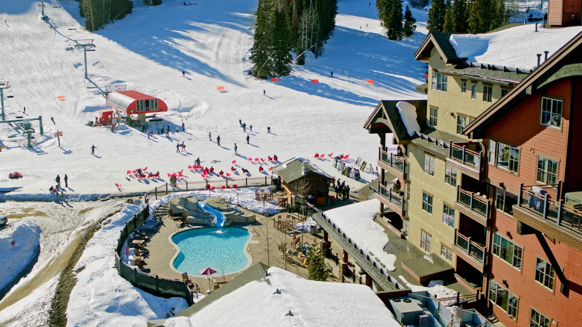 An exterior scene featuring lively ski slopes, a resort building, and a sparkling swimming pool. Skiers enjoy the slopes in winter, while the pool hints at summer relaxation. The image conveys an energetic resort atmosphere with a strong sense of activity and social gathering.