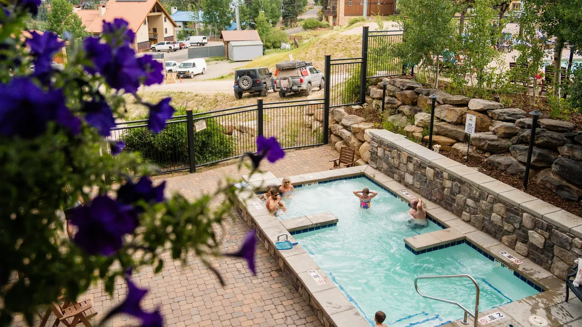 A sun-dappled communal swimming pool framed by flowers, with people relaxing and enjoying the water. The inviting leisure setting underlines the resort's vibrant, family-friendly atmosphere and opportunities for relaxation and play.